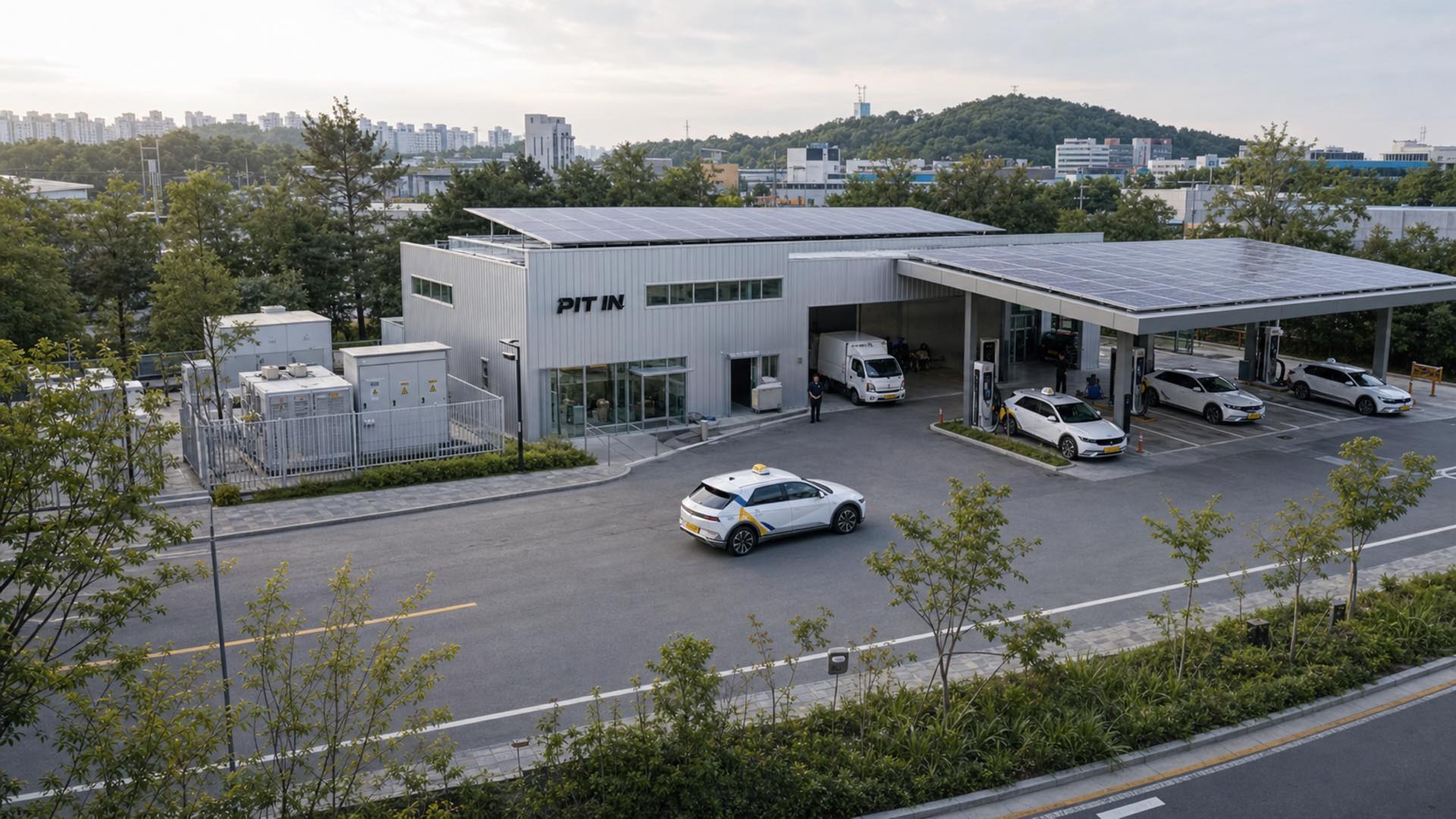 옥상과 충전 캐노피에 태양광을 얹은 PIT IN 스테이션, 충전 베이에 선 전기 택시들과 정비 베이의 전기 화물차를 담은 조감