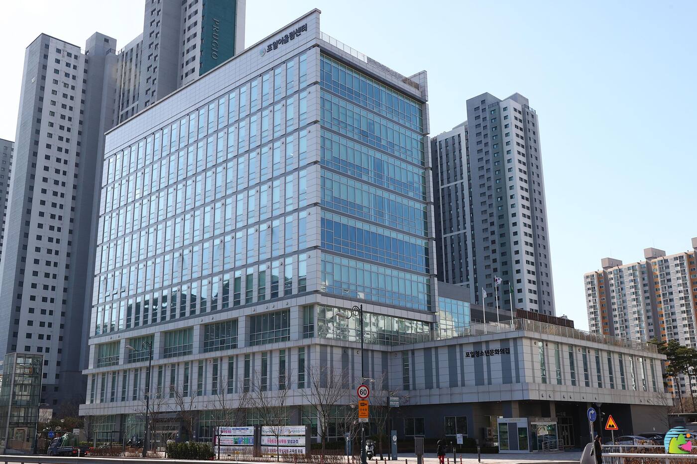 본사가 입주한 의왕 포일어울림센터 — 유리 커튼월과 은회색 패널로 마감한 건물 외관, 지붕선에 포일어울림센터 사인이 붙어 있고 뒤로 아파트 단지가 선다